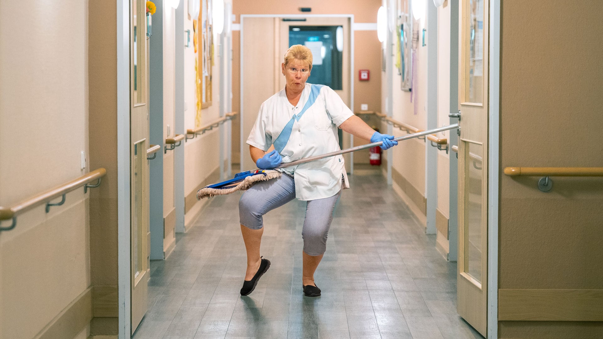 Eine Frau mit konzentriertem Gesichtsausdruck trägt blau-weiße Kleidung und hält einen Mopp in die Höhe.